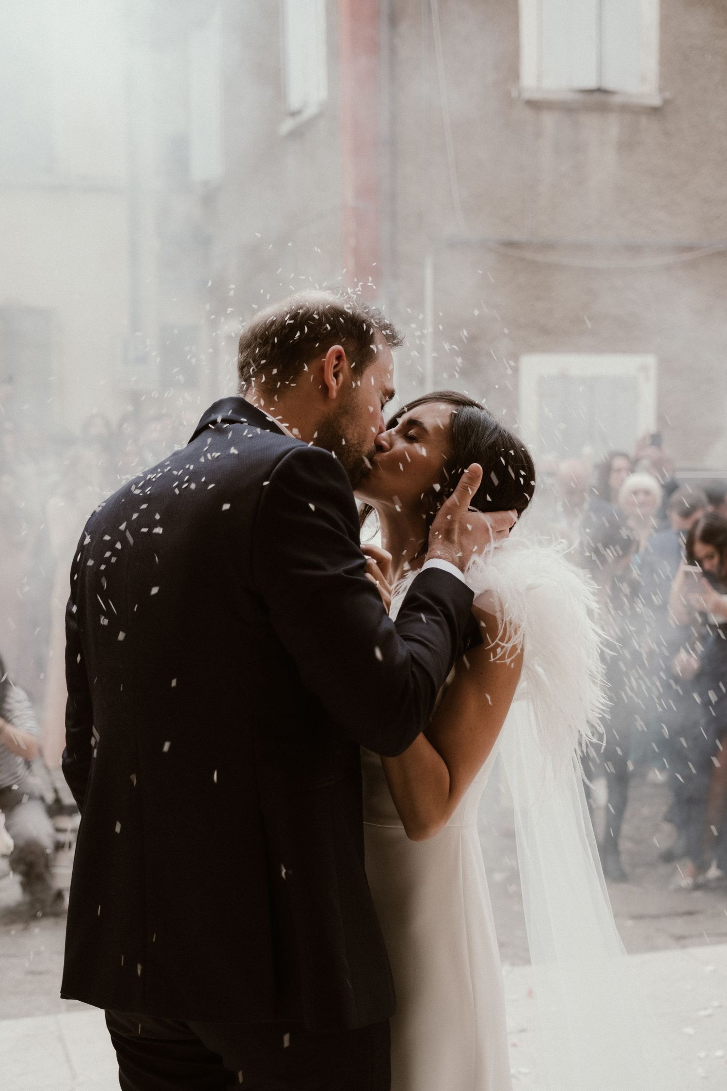 Newlyweds share a romantic kiss surrounded by falling confetti outside a church on their wedding day.
