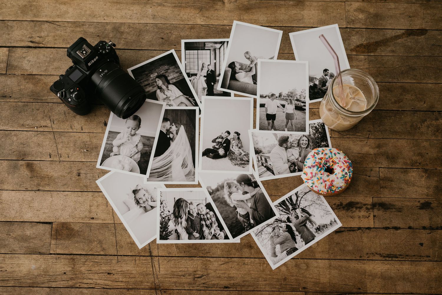 Vintage black and white photographs scattered on a rustic wooden table surface next to an old camera.