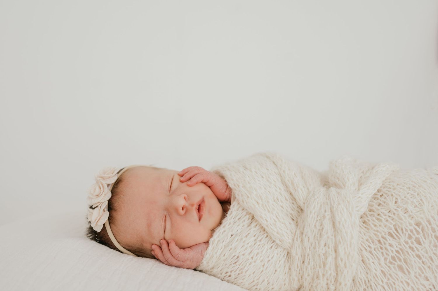 A baby wearing white knit clothing sleeps peacefully on a soft textured blanket.