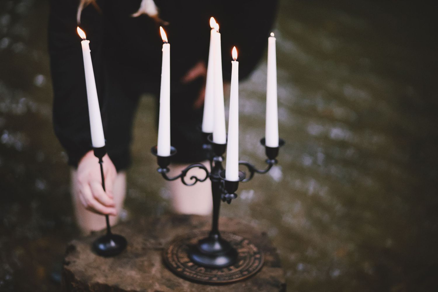 Black candelabra with five white lit candles on stone surface near water.