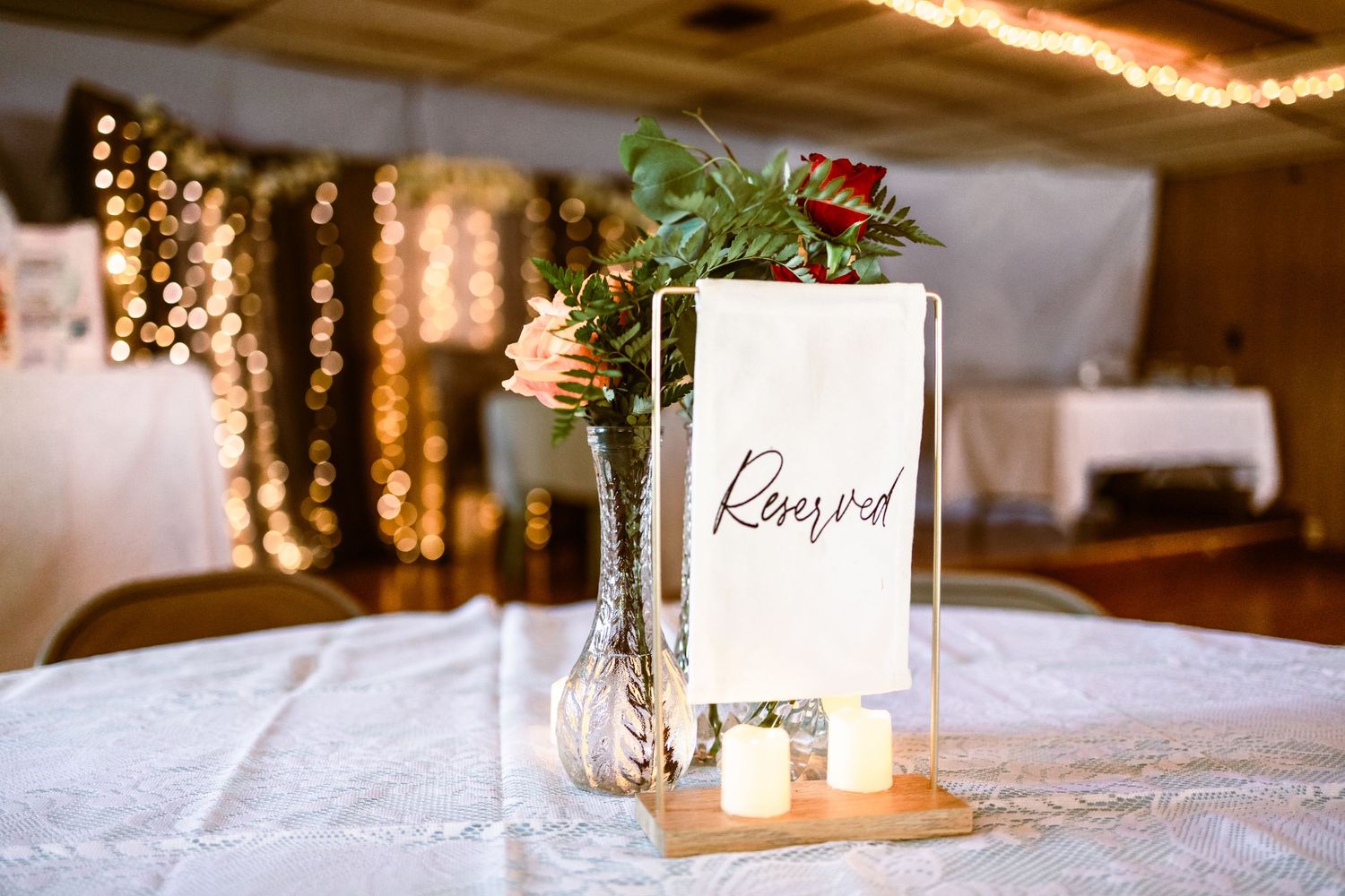 Elegant wedding table with a reserved sign, floral centerpiece, and twinkling lights in the background.