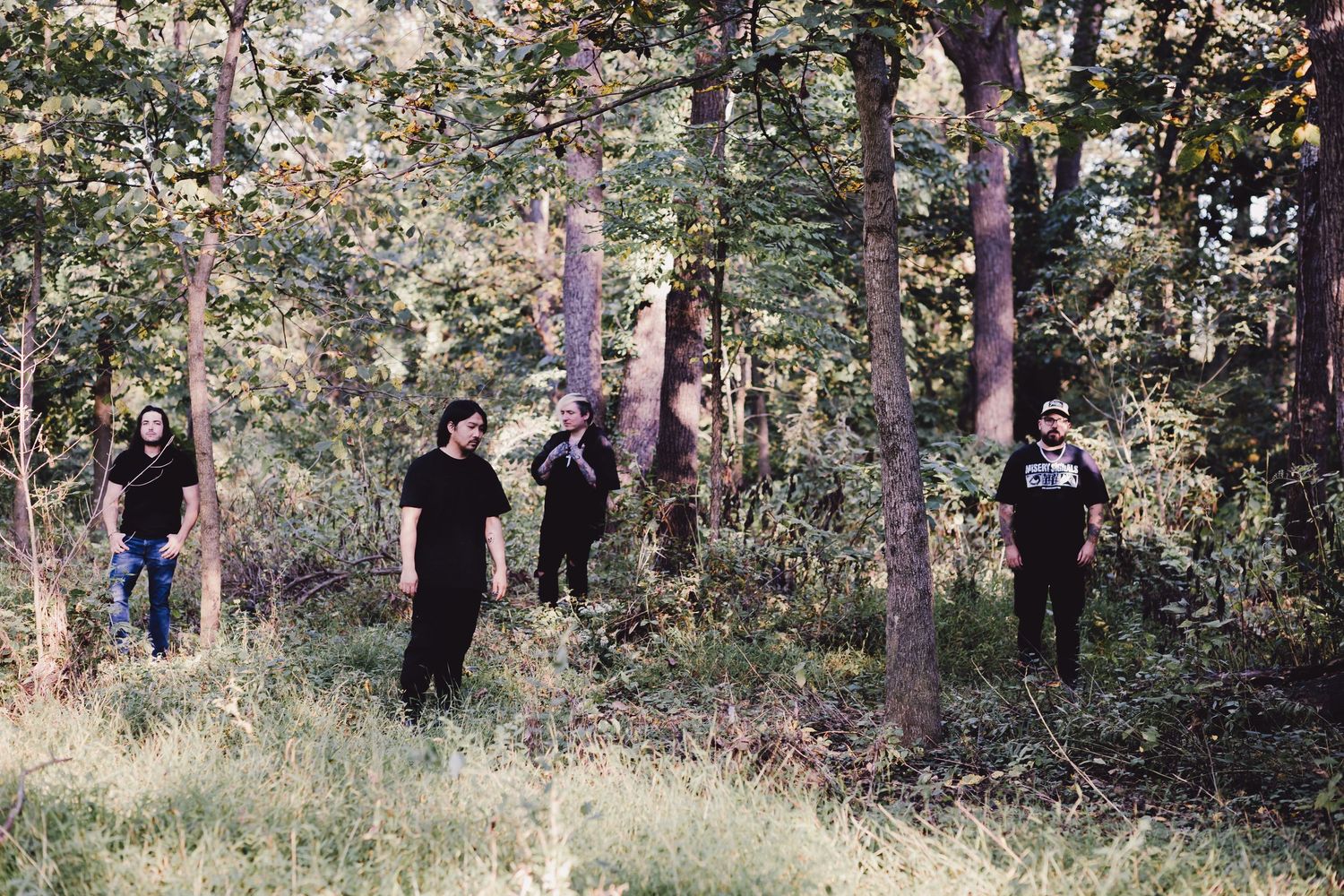 Four people standing among trees in a forest during a band photo shoot.