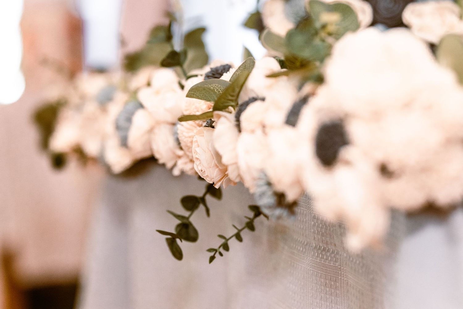 Close-up of elegant white roses and eucalyptus floral arrangement decorating a wedding ceremony aisle.