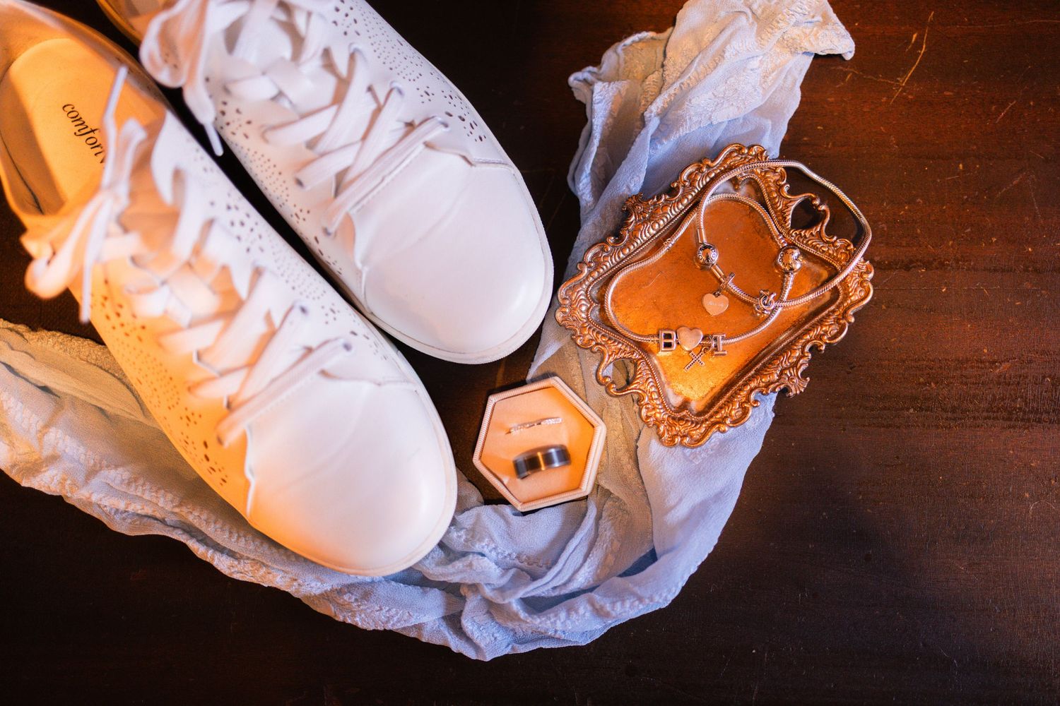 White sneakers and wedding rings in an orange hexagonal box with jewelry on a dark wood surface.