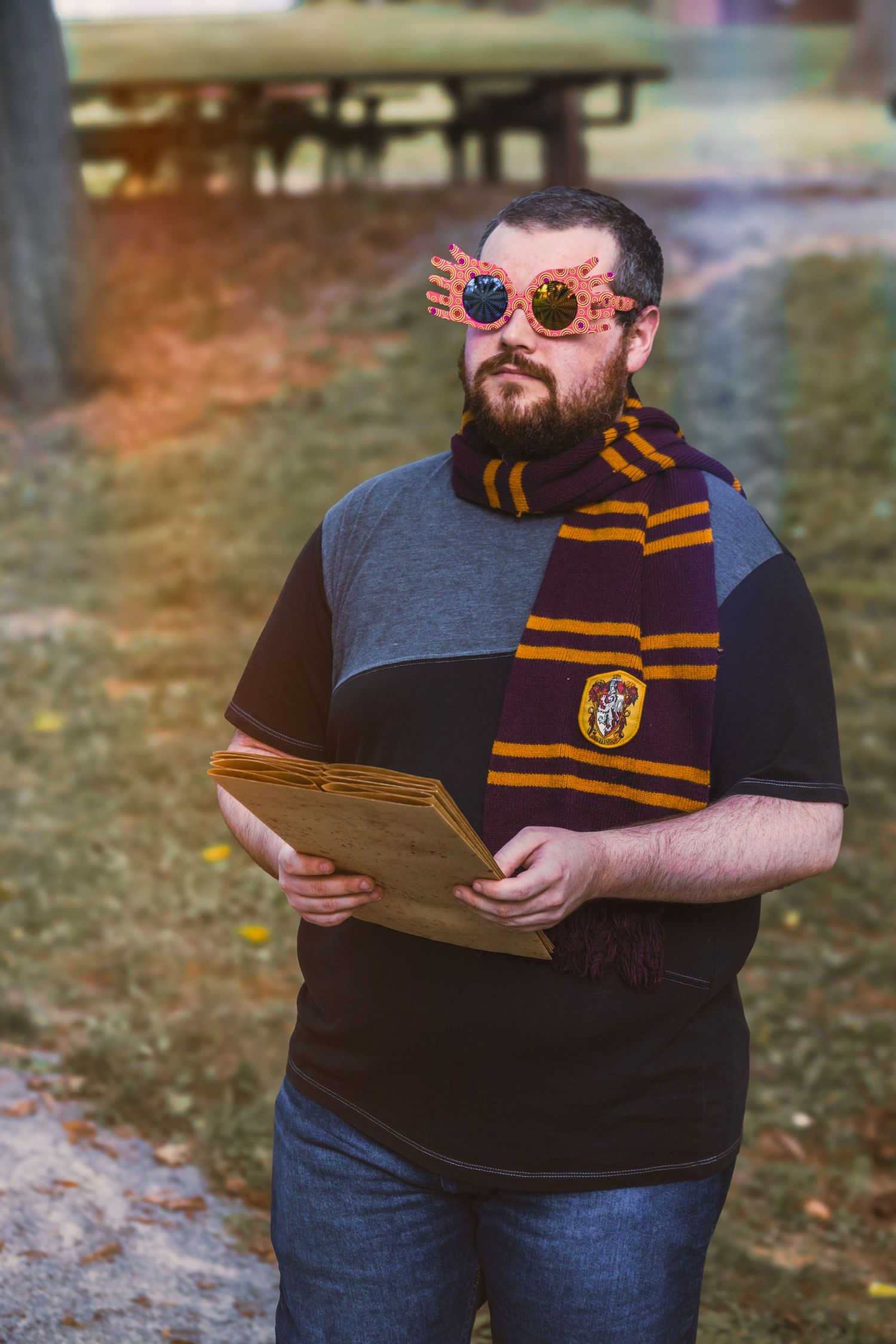 Man wearing Gryffindor scarf, novelty glasses, and holding a book outdoors in a Harry Potter-themed costume.