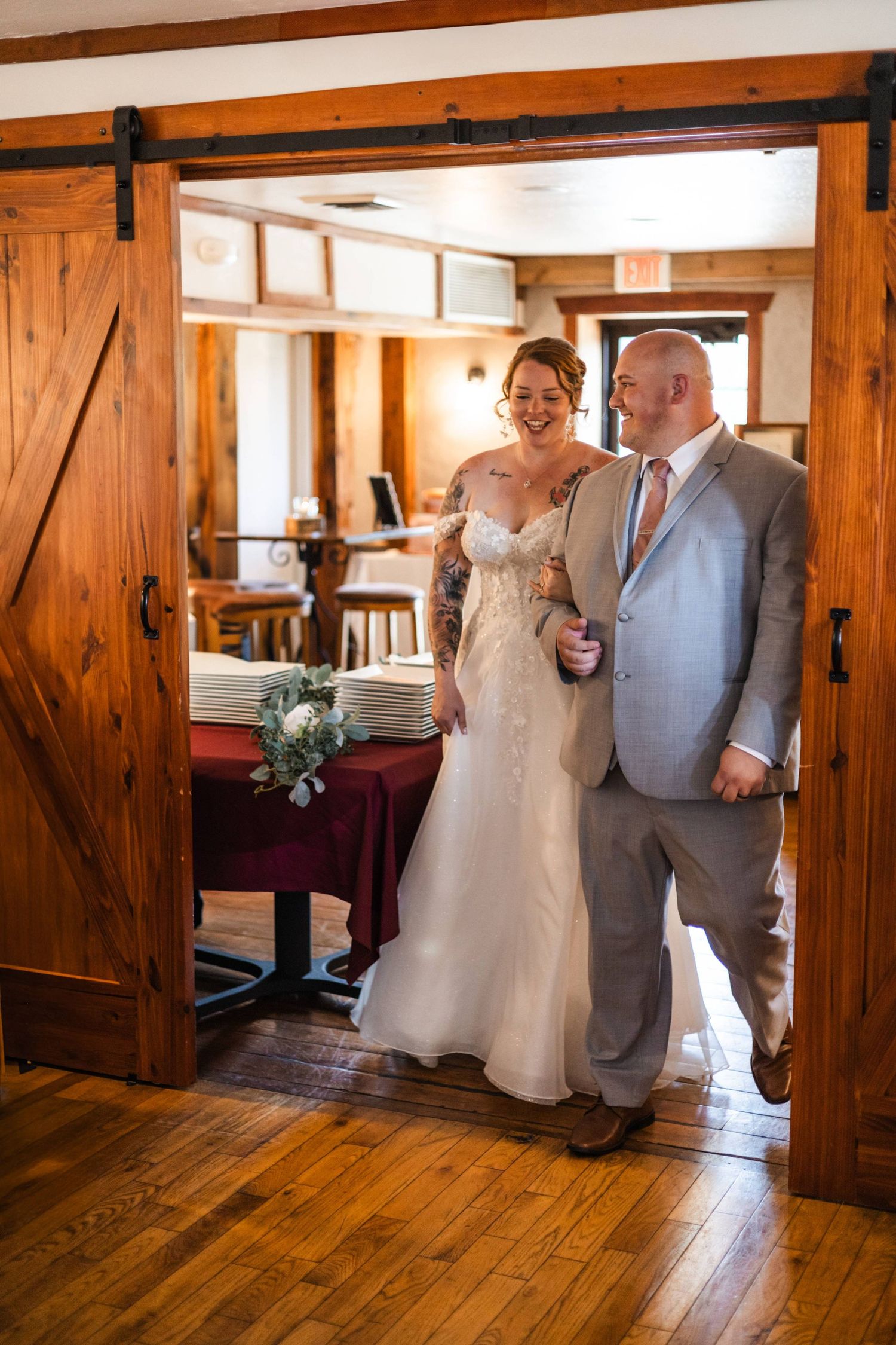 Bride and groom laughing as they enter a rustic barn wedding reception through wooden doors.