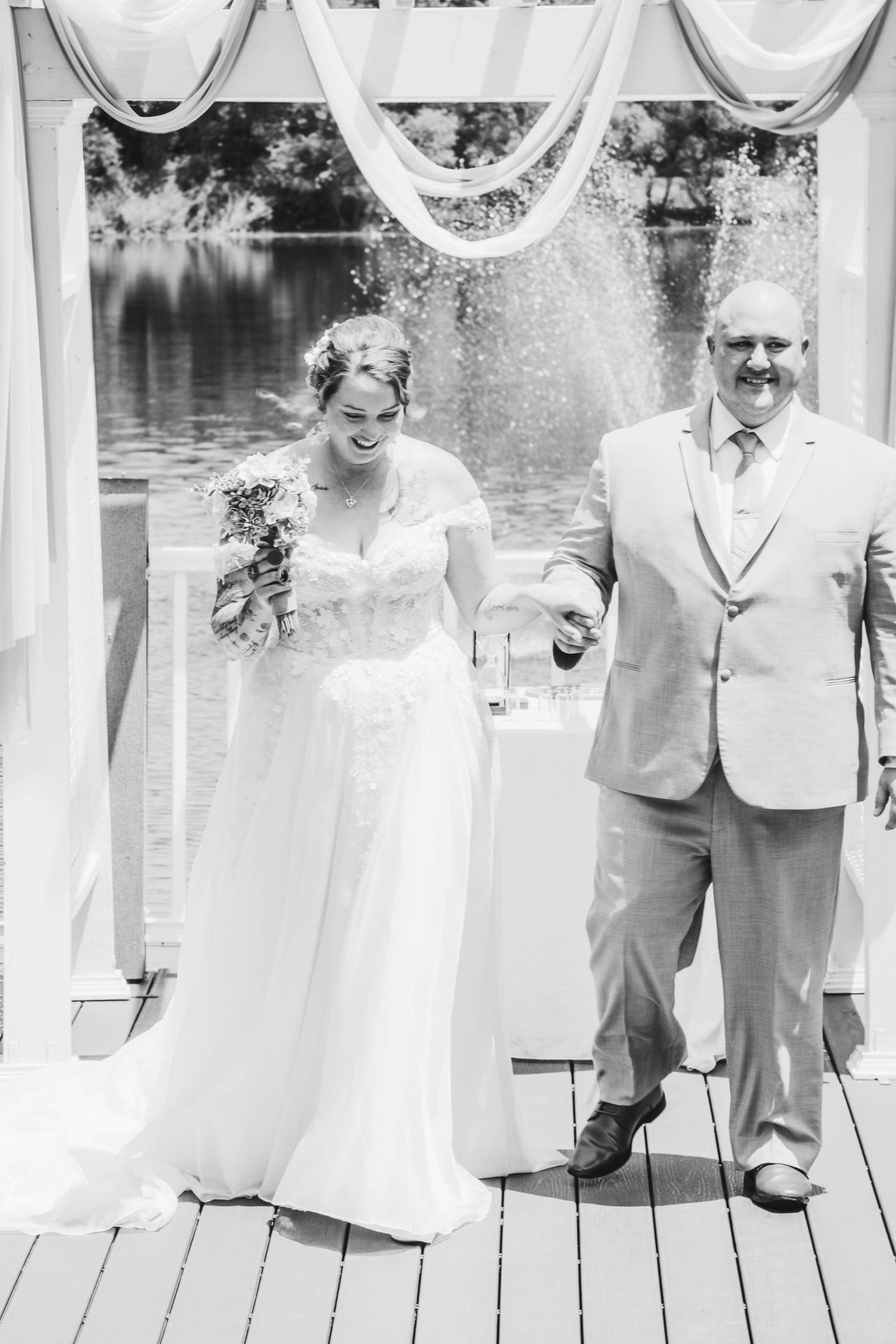 Black and white photo of a smiling bride and groom exiting their outdoor wedding ceremony.