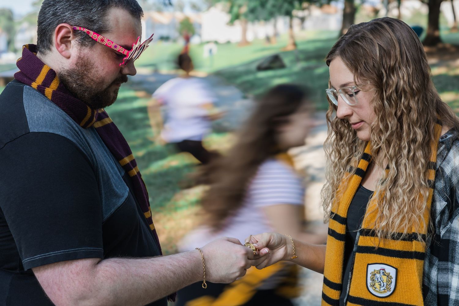 Two Harry Potter fans in Gryffindor and Hufflepuff scarves examine an object outdoors at a themed event.