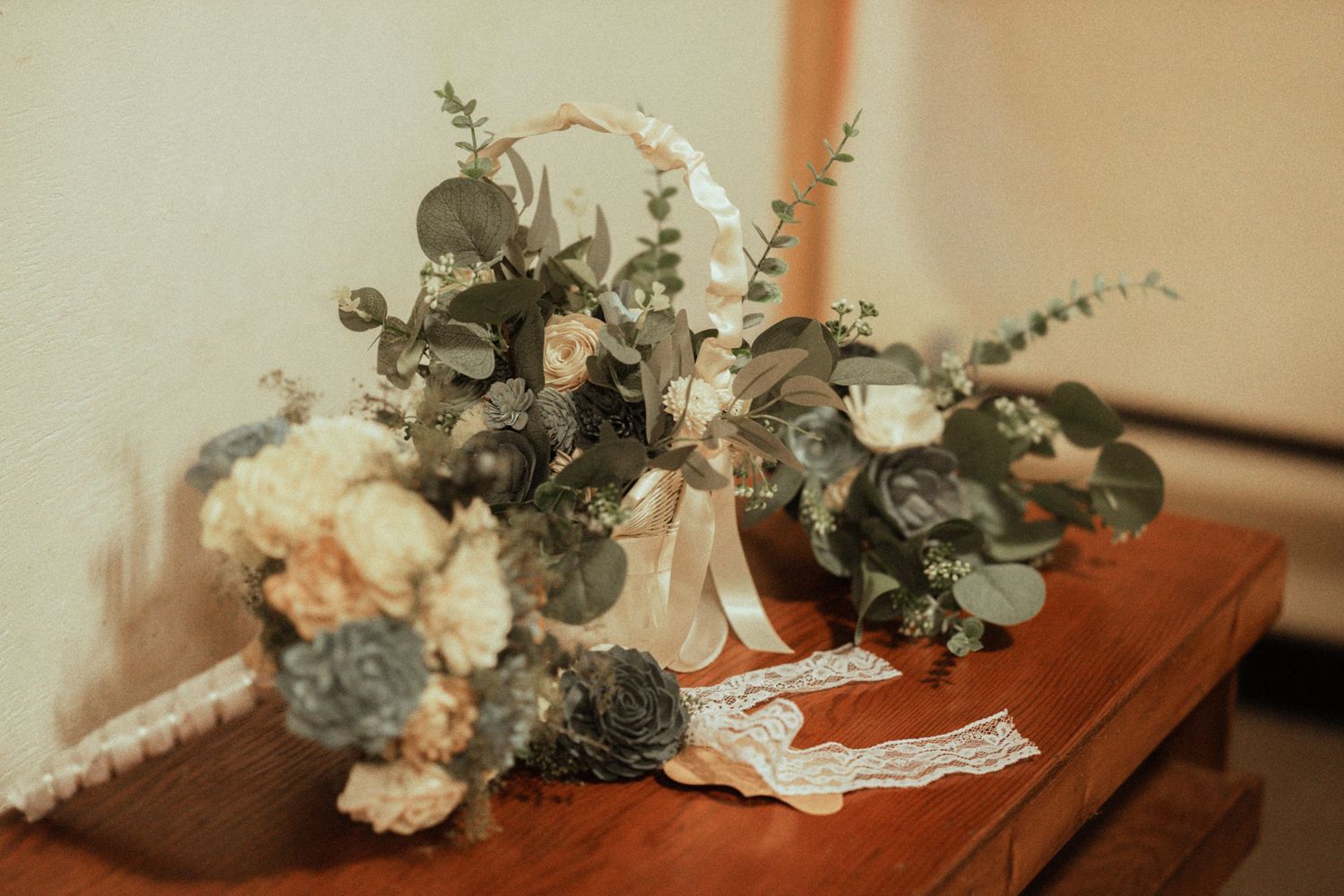 Rustic wedding bouquets with eucalyptus, dusty blue and blush flowers displayed on a wooden table.