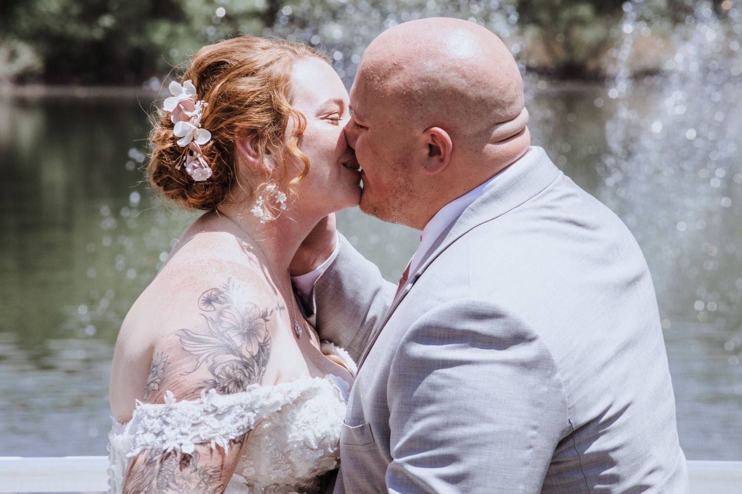 Bride and groom share a romantic kiss in front of a fountain on their wedding day.