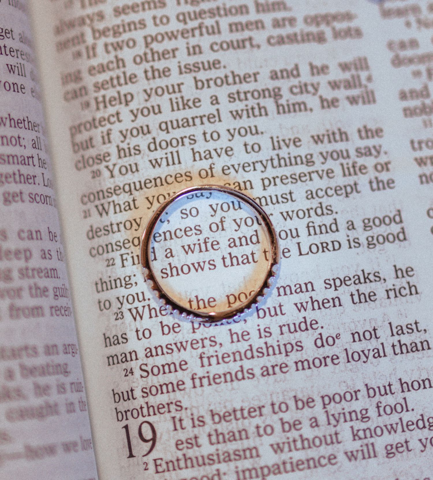 A gold wedding ring resting on an open Bible page with Proverbs text visible beneath it.
