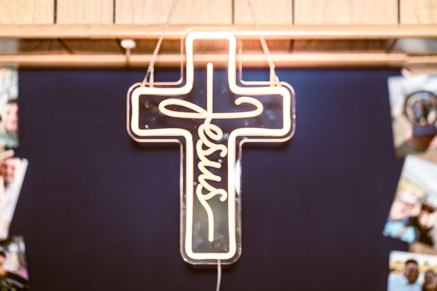 Illuminated neon cross sign with Jesus written in cursive script, glowing against a dark blue background.