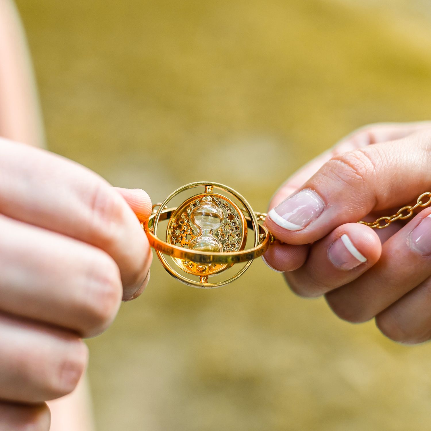 Hands holding a gold Time-Turner hourglass necklace, a iconic Harry Potter magical artifact prop.