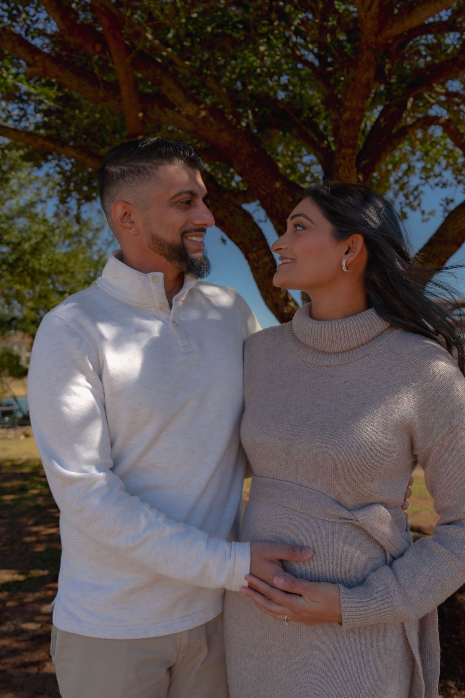 Smiling couple sharing tender maternity moment outdoors with man touching pregnant belly.