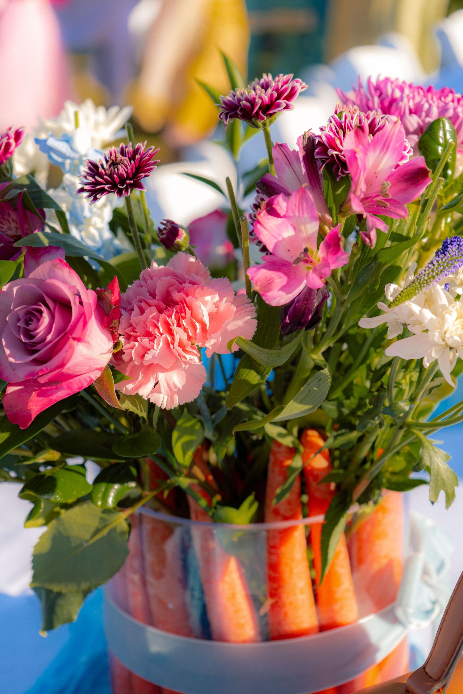 Vibrant baby shower floral centerpiece with pink roses, carnations, and purple chrysanthemums in a vase with carrots.