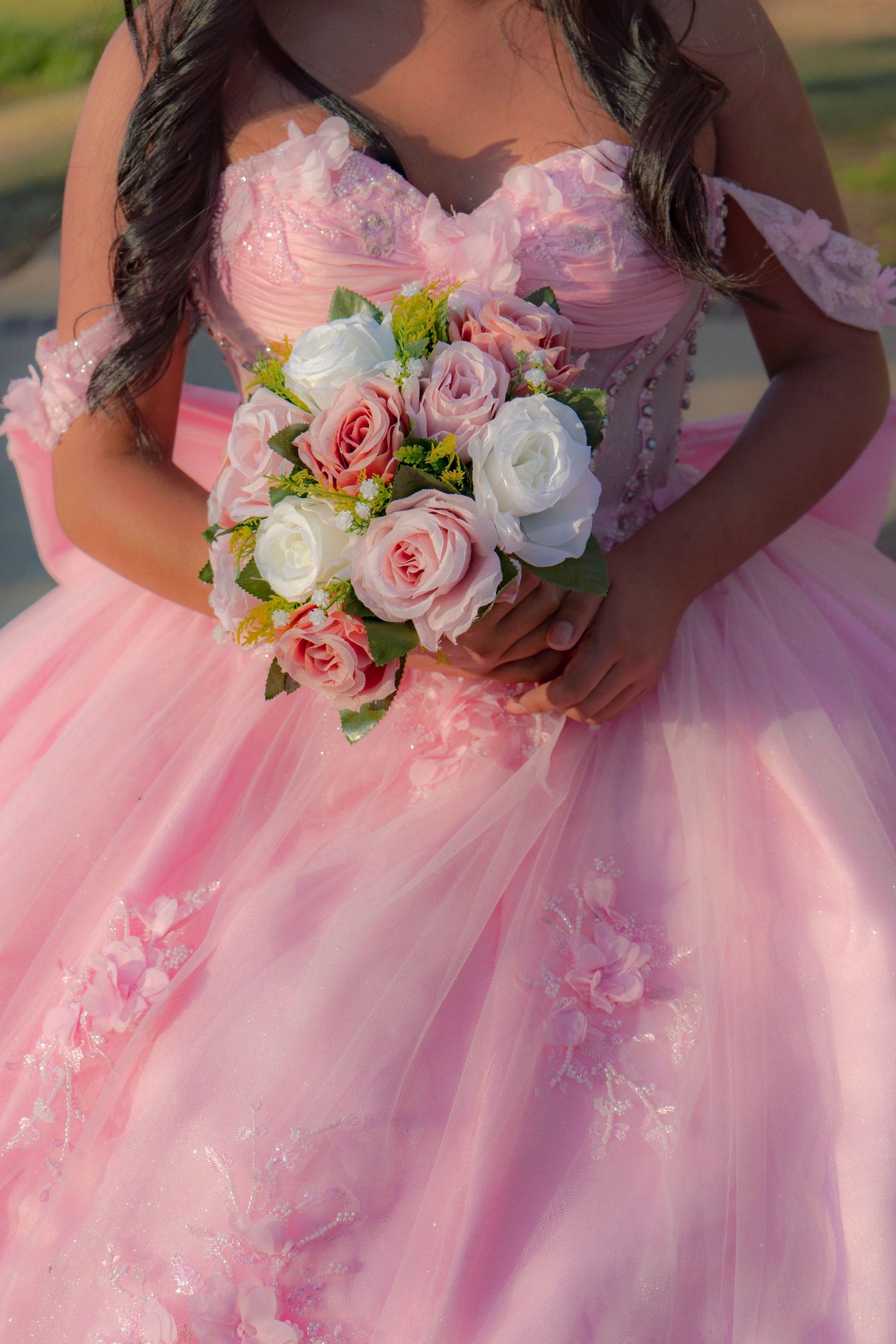 Close-up of quinceañera girl in pink ball gown holding a beautiful bouquet of pink and white roses.