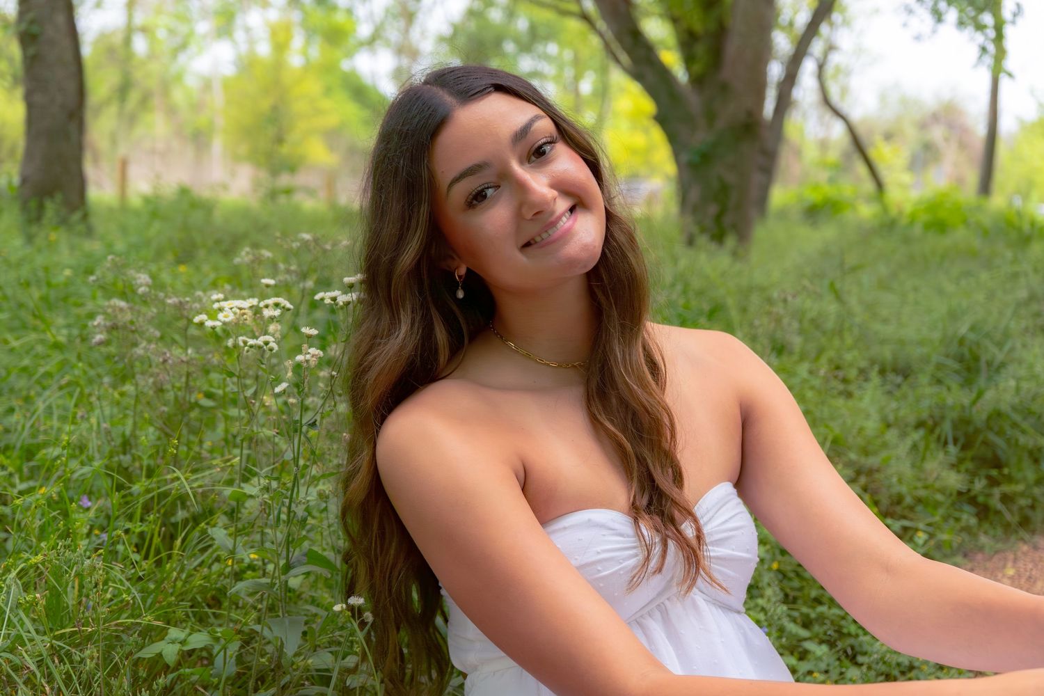 Young woman in white strapless top smiling outdoors among green foliage and wildflowers.
