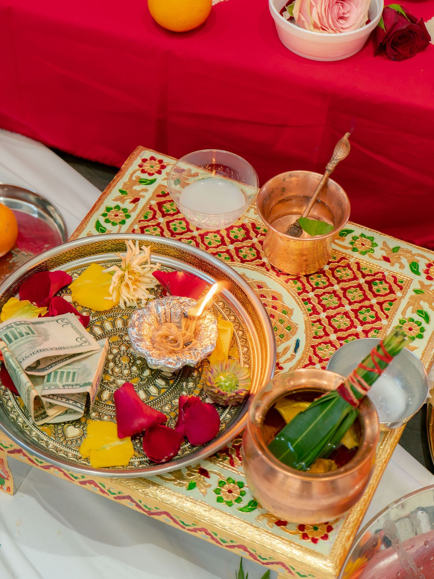 Decorative Indian puja thali with rose petals, diya, copper vessels, and offerings on ornate gold tray.