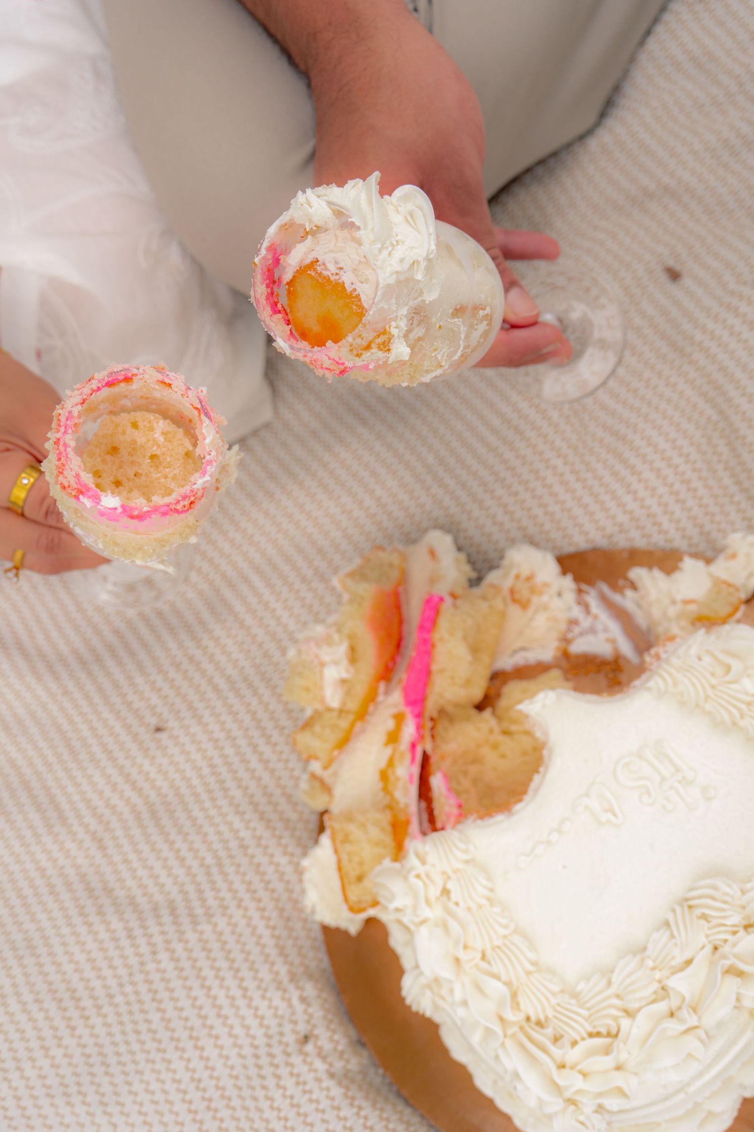 Gender reveal cake cut open showing pink filling, with pieces held up by couple sitting on white blanket.