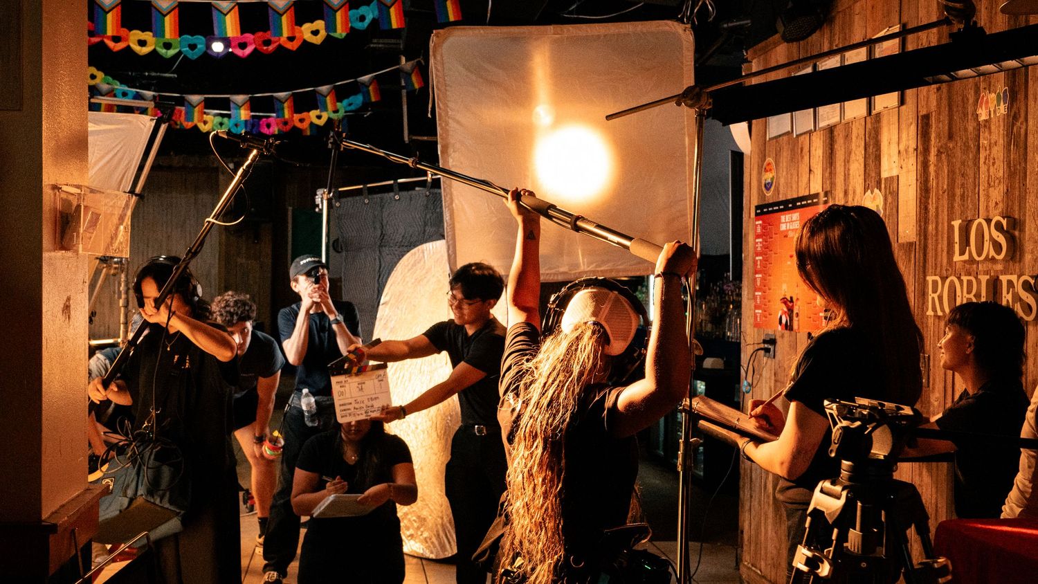 Busy film crew working with boom mic and lights on a colorful indoor production set.