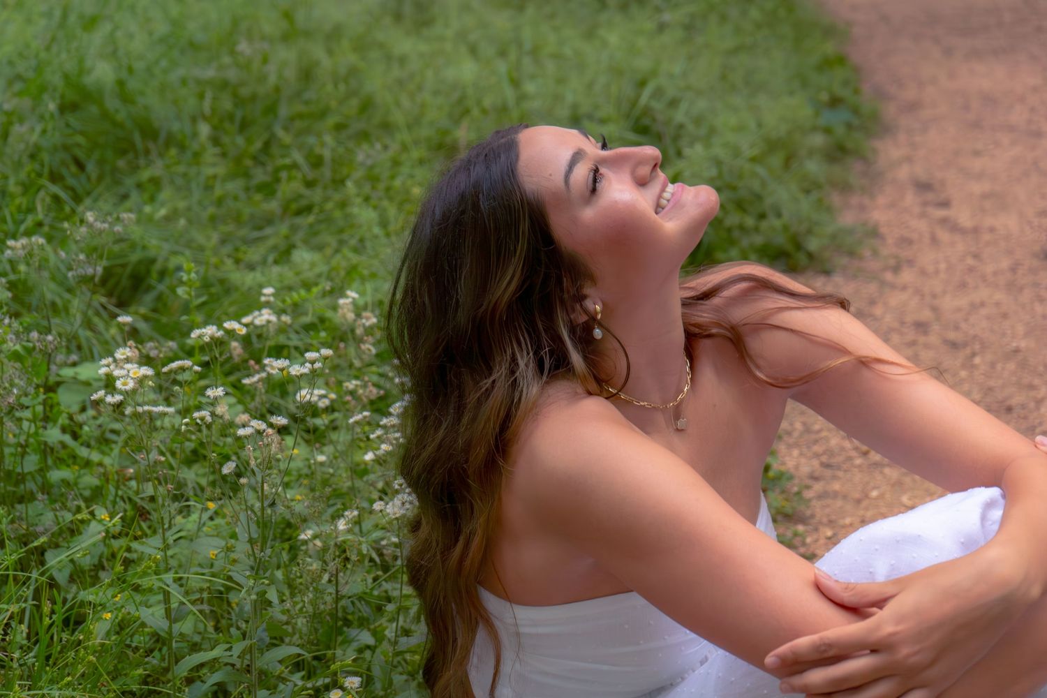 A young woman in a white dress laughs joyfully outdoors, surrounded by lush green grass and wildflowers.