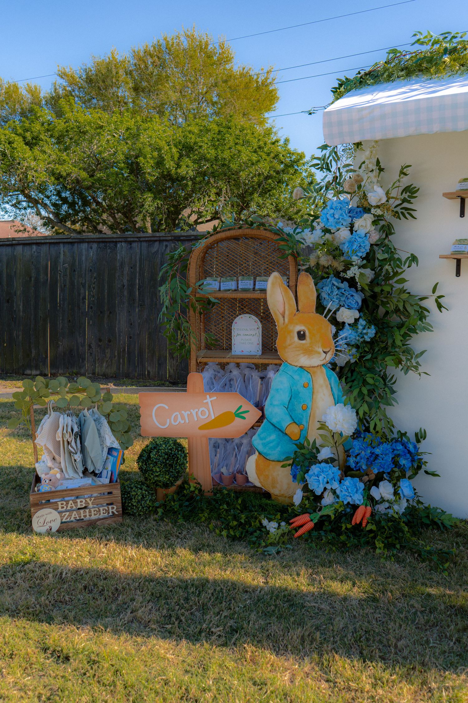 Peter Rabbit themed baby shower outdoor decoration with blue hydrangeas, carrot sign, and wicker shelf display.