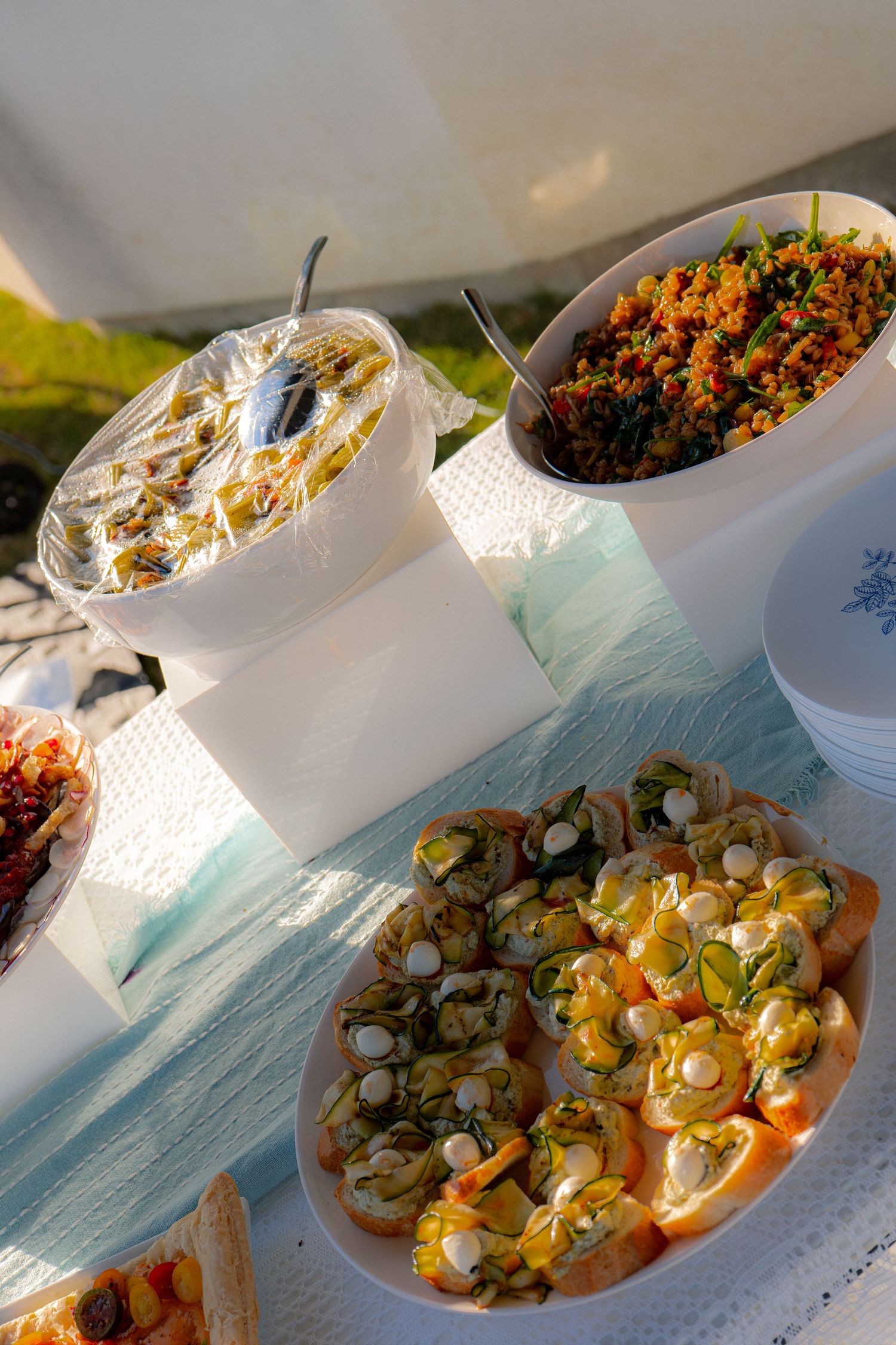 Elegant baby shower appetizer spread with canapes, grain salad, and assorted finger foods on a white tablecloth outdoors.