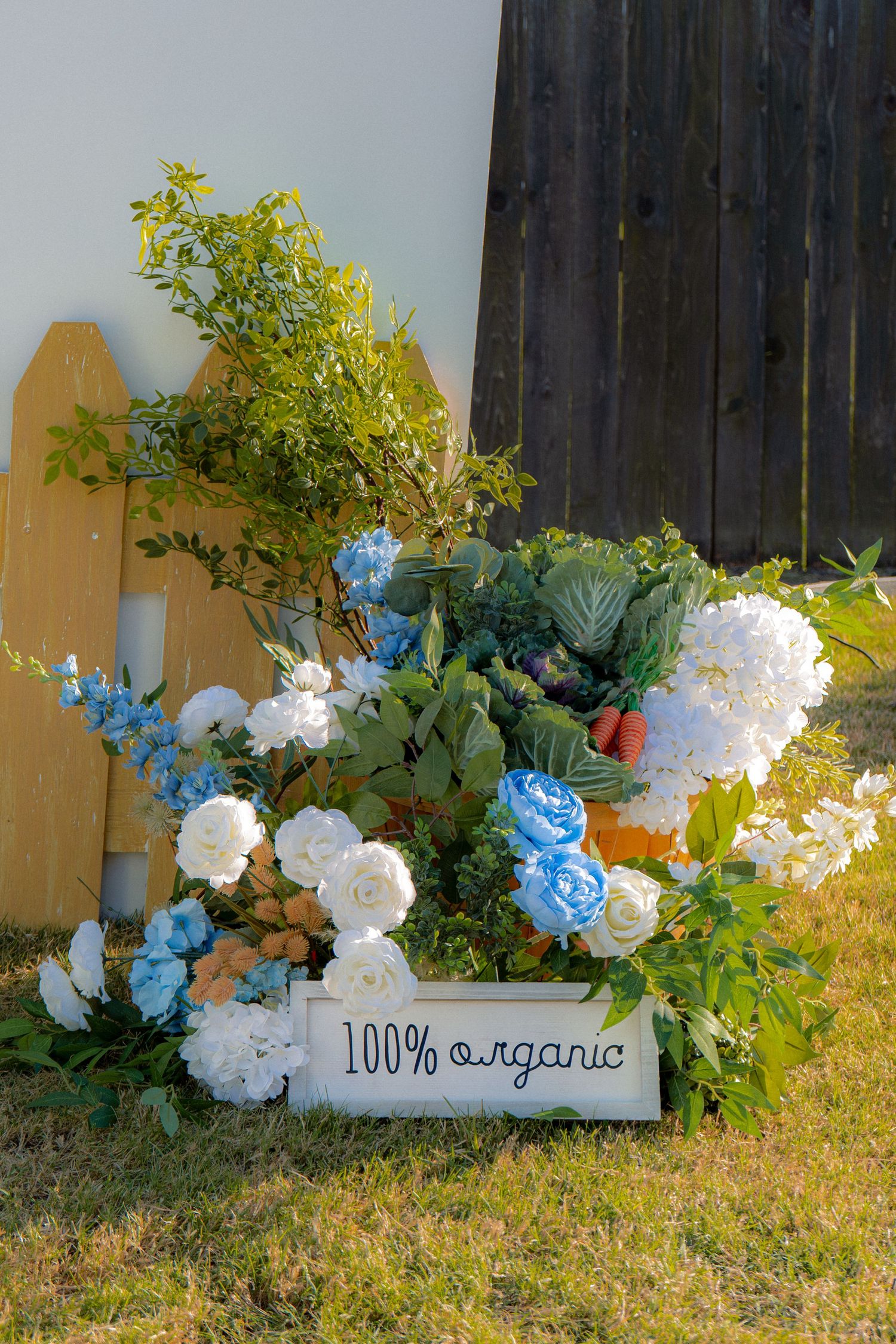 Decorative garden display with blue and white flowers and a 100% organic wooden sign outdoors.