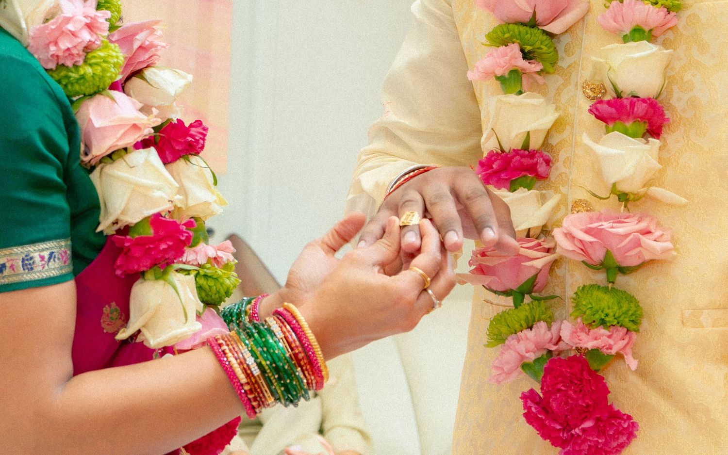 Close-up of Indian wedding ring exchange ceremony with colorful floral garlands and bride wearing traditional green bangles.