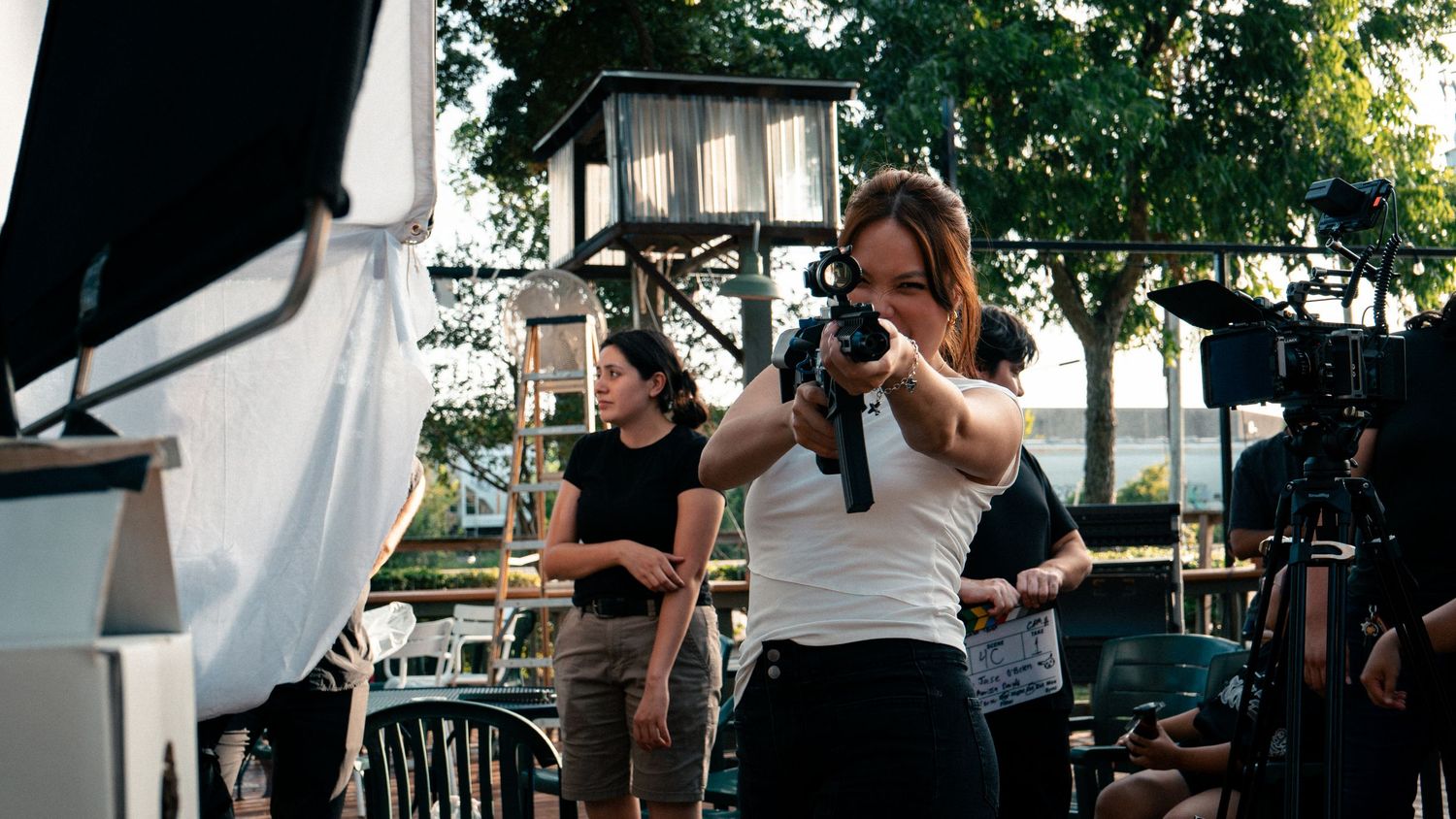 A cinematographer films outdoors on a sunny day while a crew member assists on set.