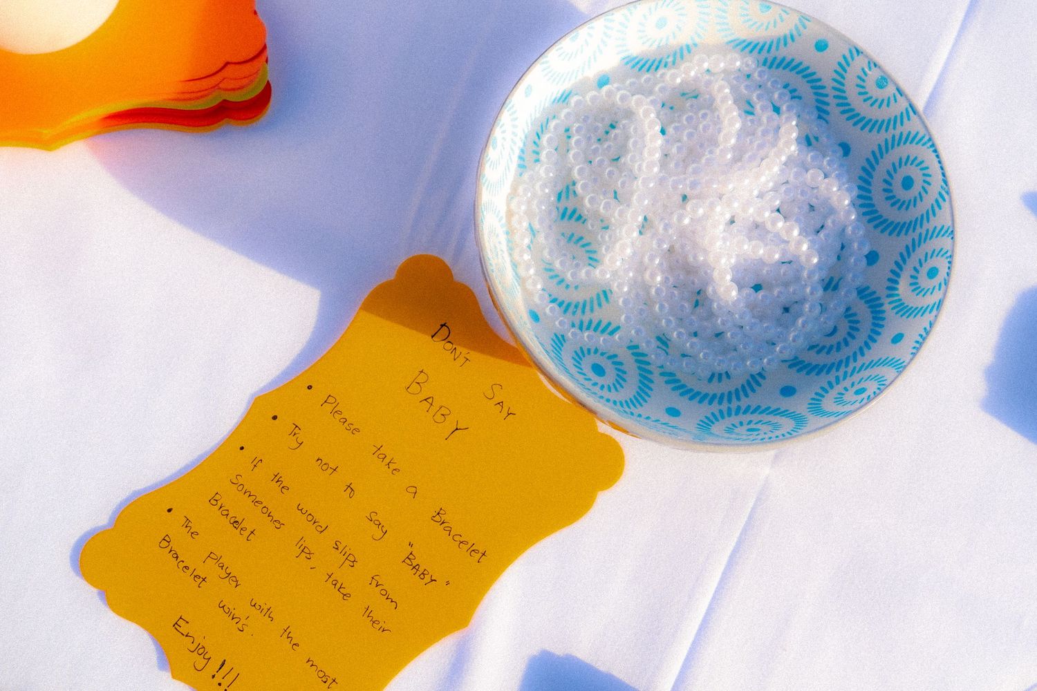 Baby shower place setting with a blue patterned bowl, orange menu card with handwritten text on white tablecloth.