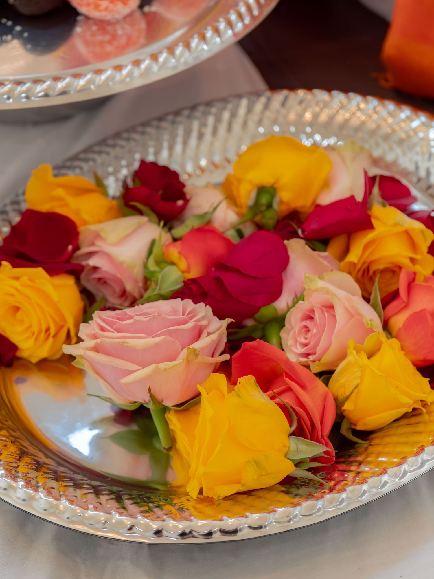 Colorful assorted roses in pink, yellow, red, and orange arranged on a silver decorative plate centerpiece.