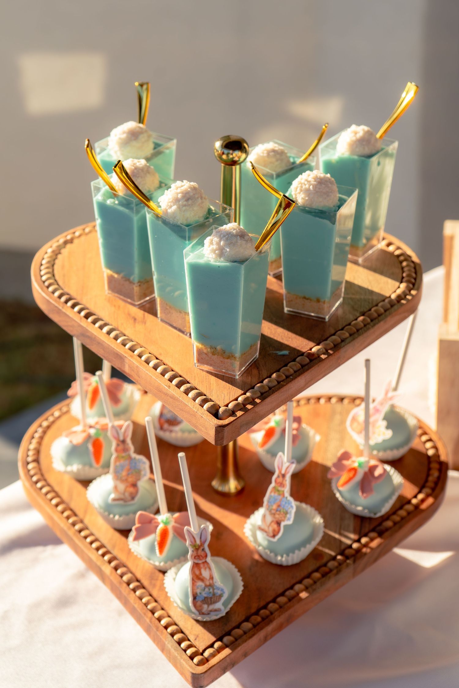 Two-tier wooden dessert stand with blue mousse cups and bunny cake pops for a baby shower.