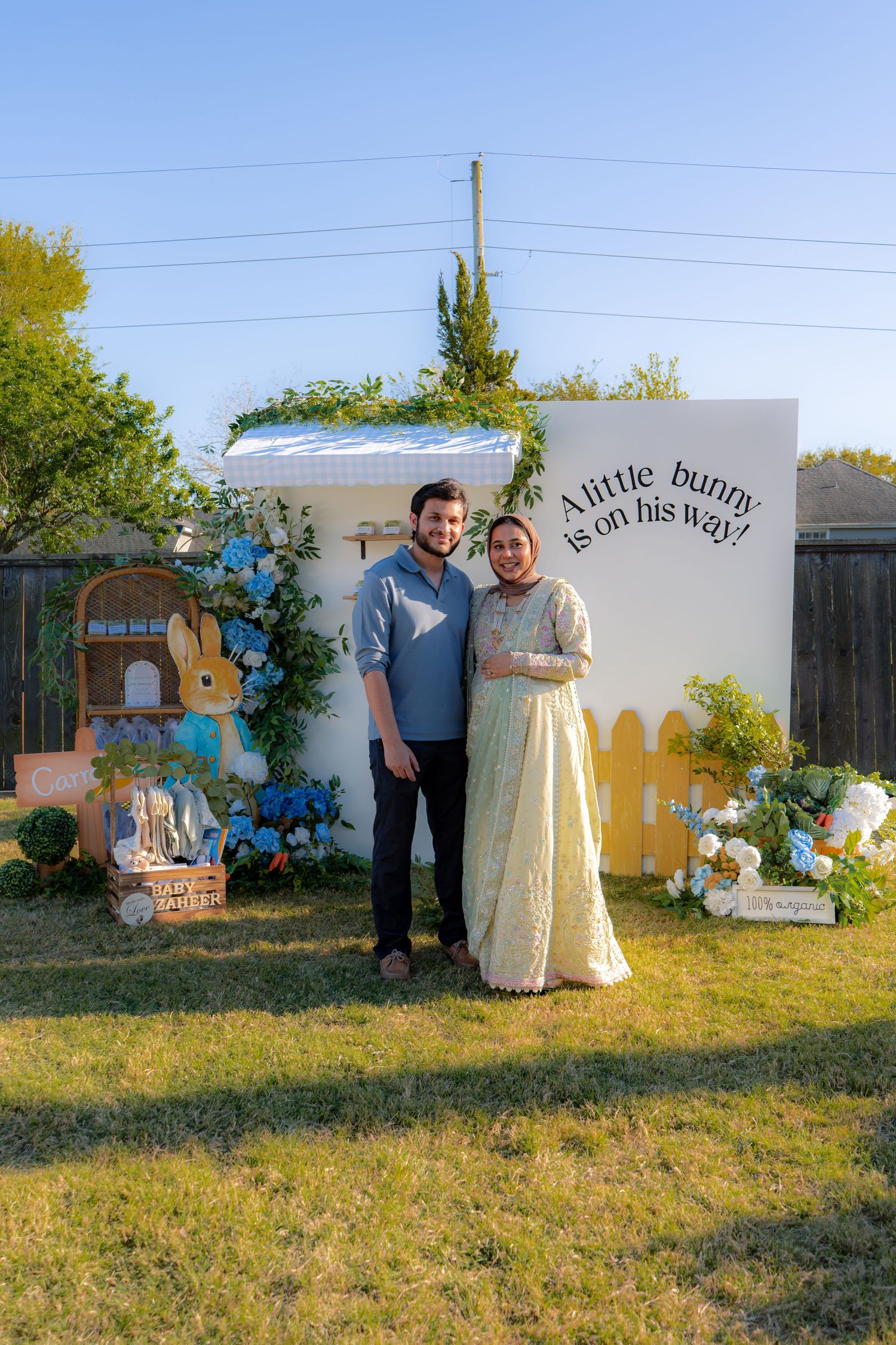 Couple posing at Peter Rabbit themed baby shower with blue floral decorations and bunny signage.