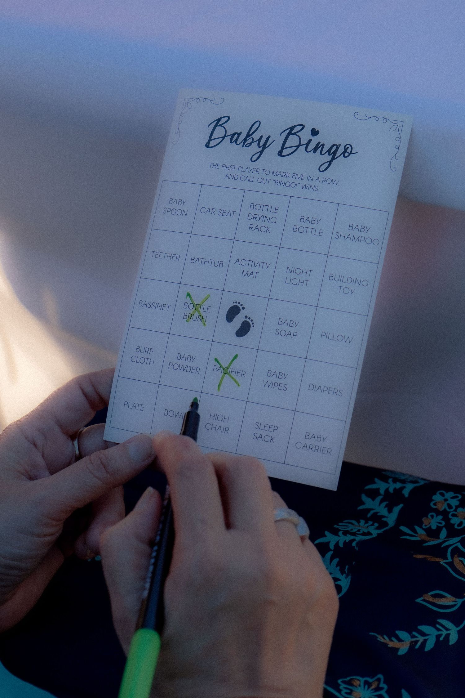 Hands marking a Baby Bingo card with a black marker at a baby shower game.