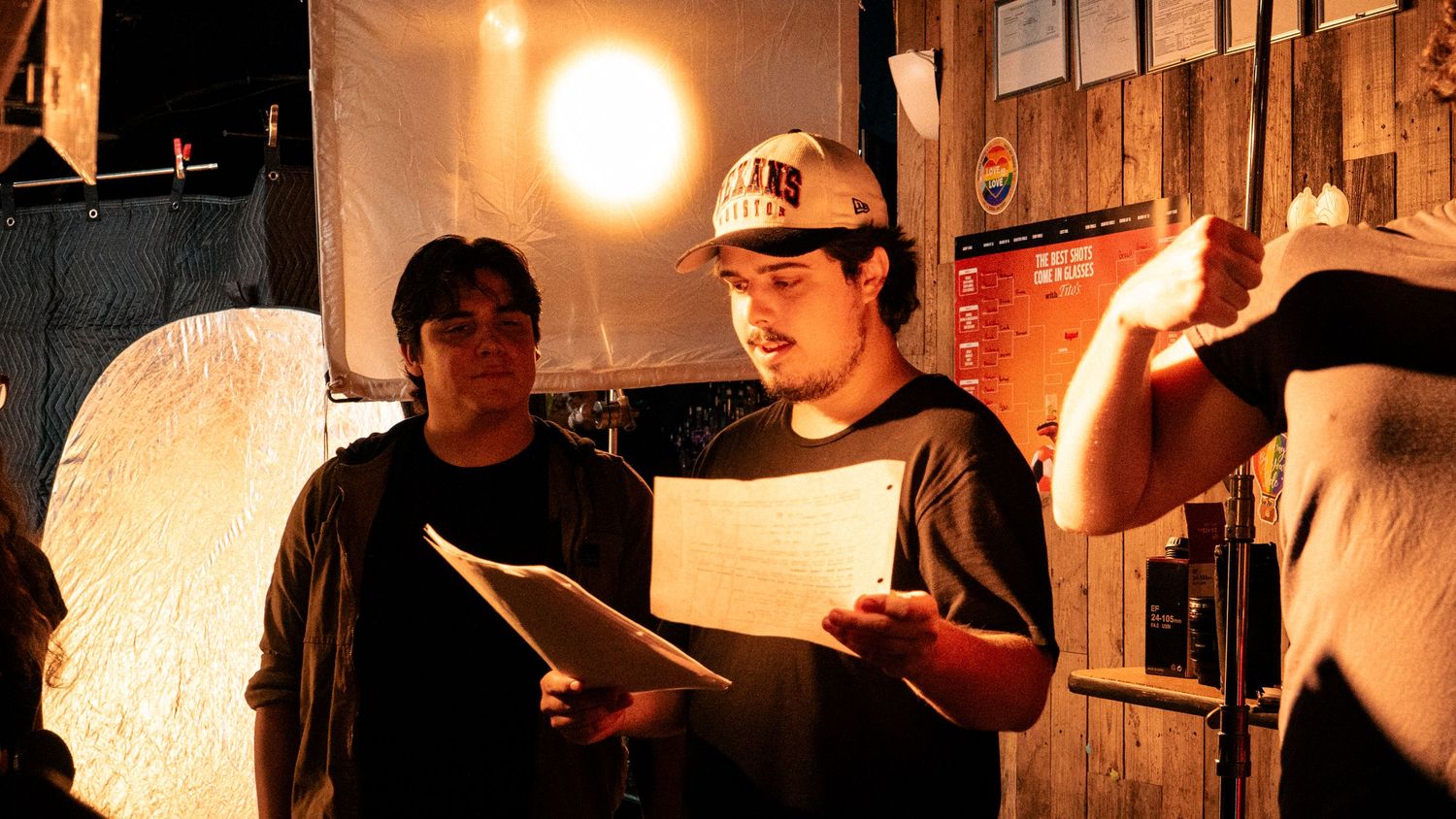 Two people reading scripts under stage lighting in a dimly lit theater rehearsal space.