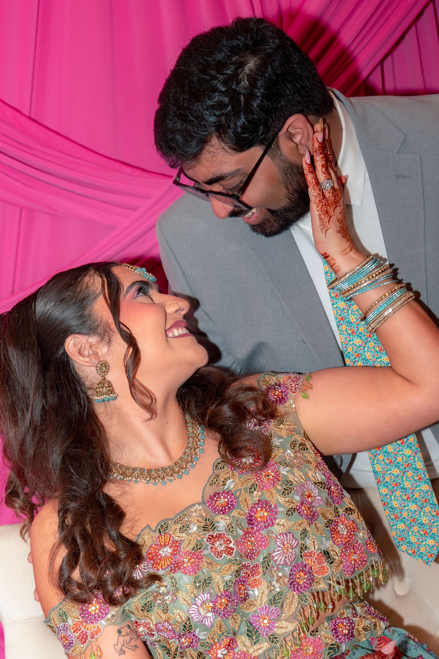 A couple in traditional Indian attire share a romantic moment, with the woman adorned in mehndi and colorful bangles.