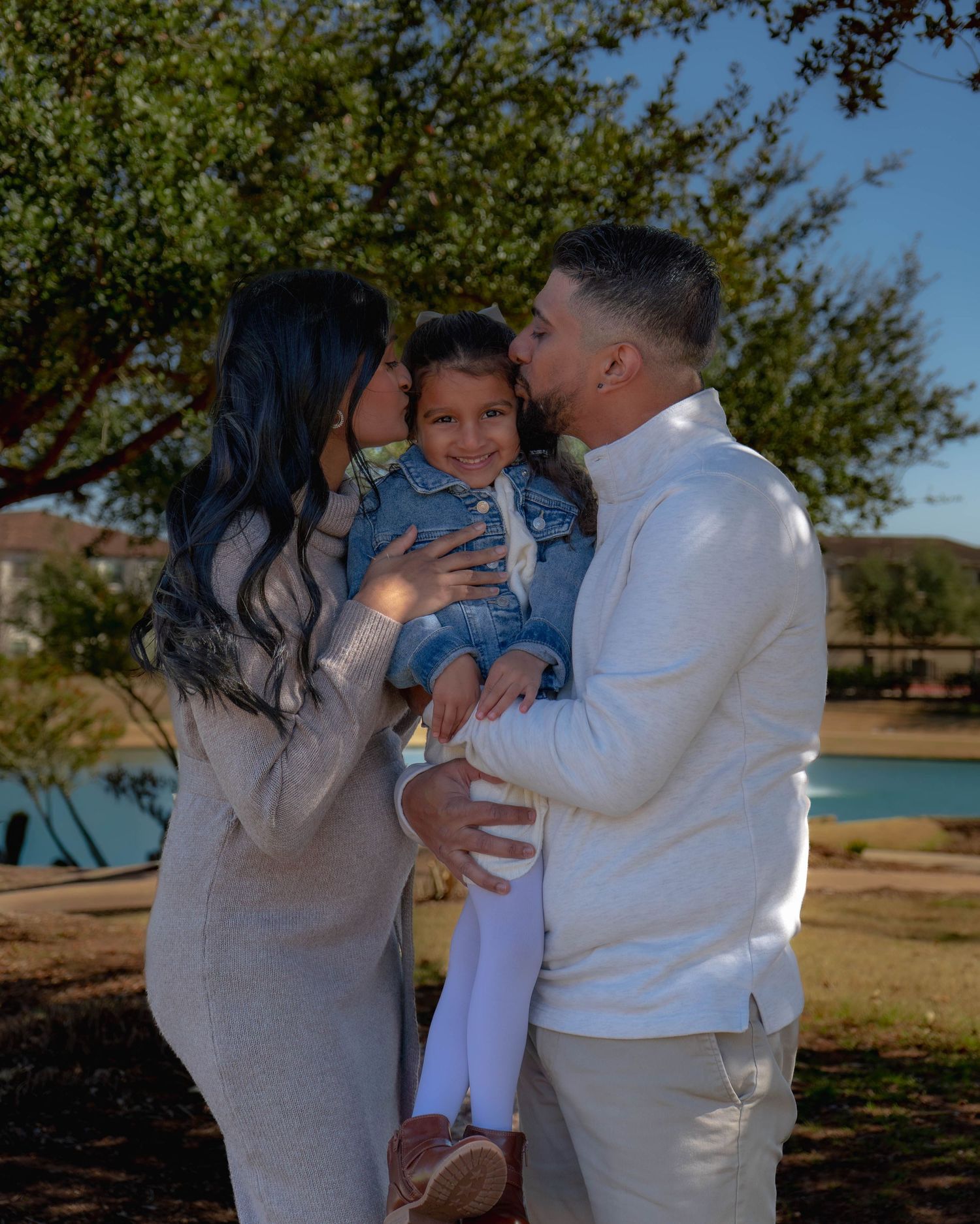 Family maternity photo with couple kissing toddler wearing denim Big Sis jacket outdoors.