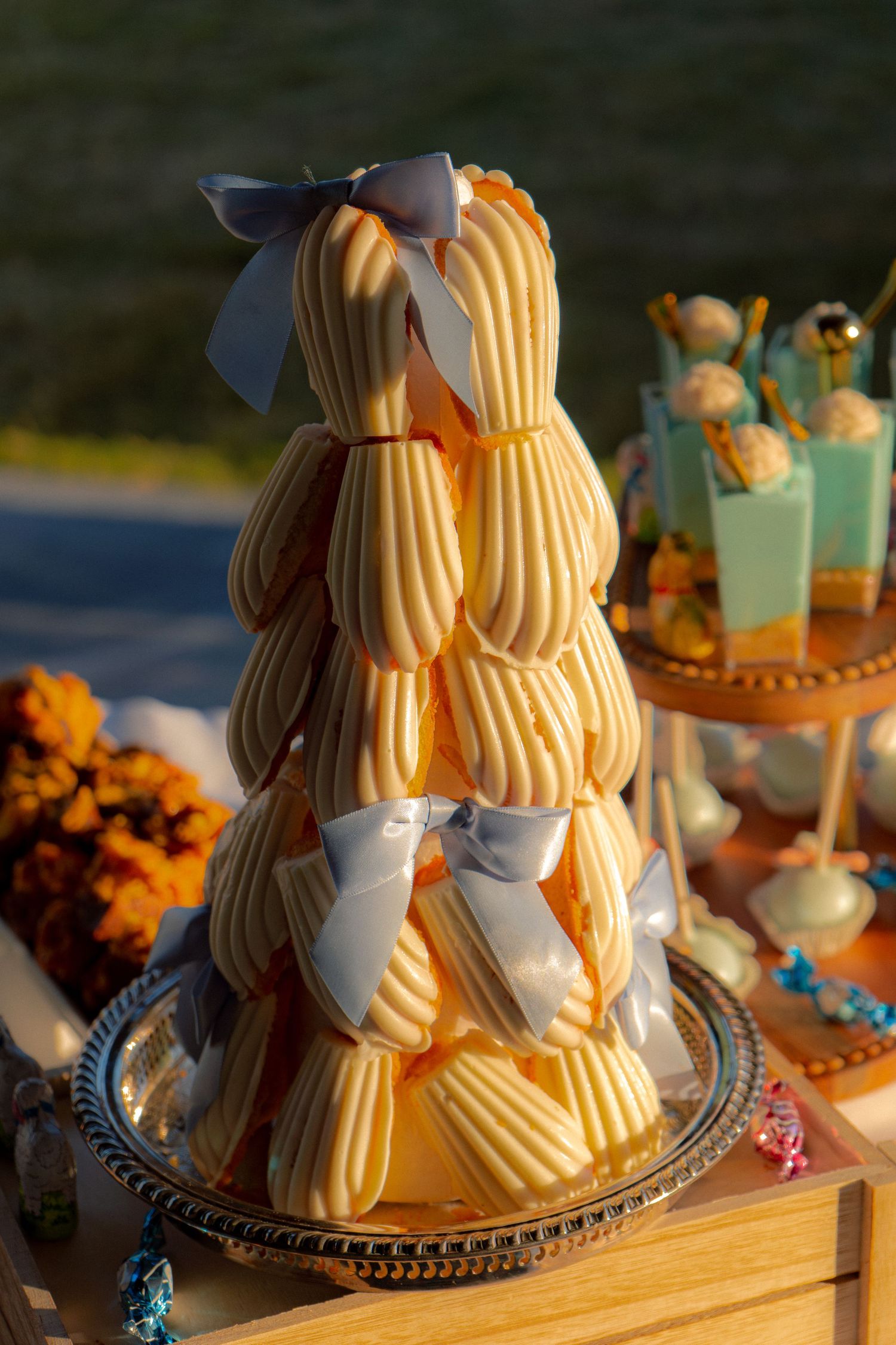 Cream puff tower with blue bows displayed on a wooden crate at an outdoor party.