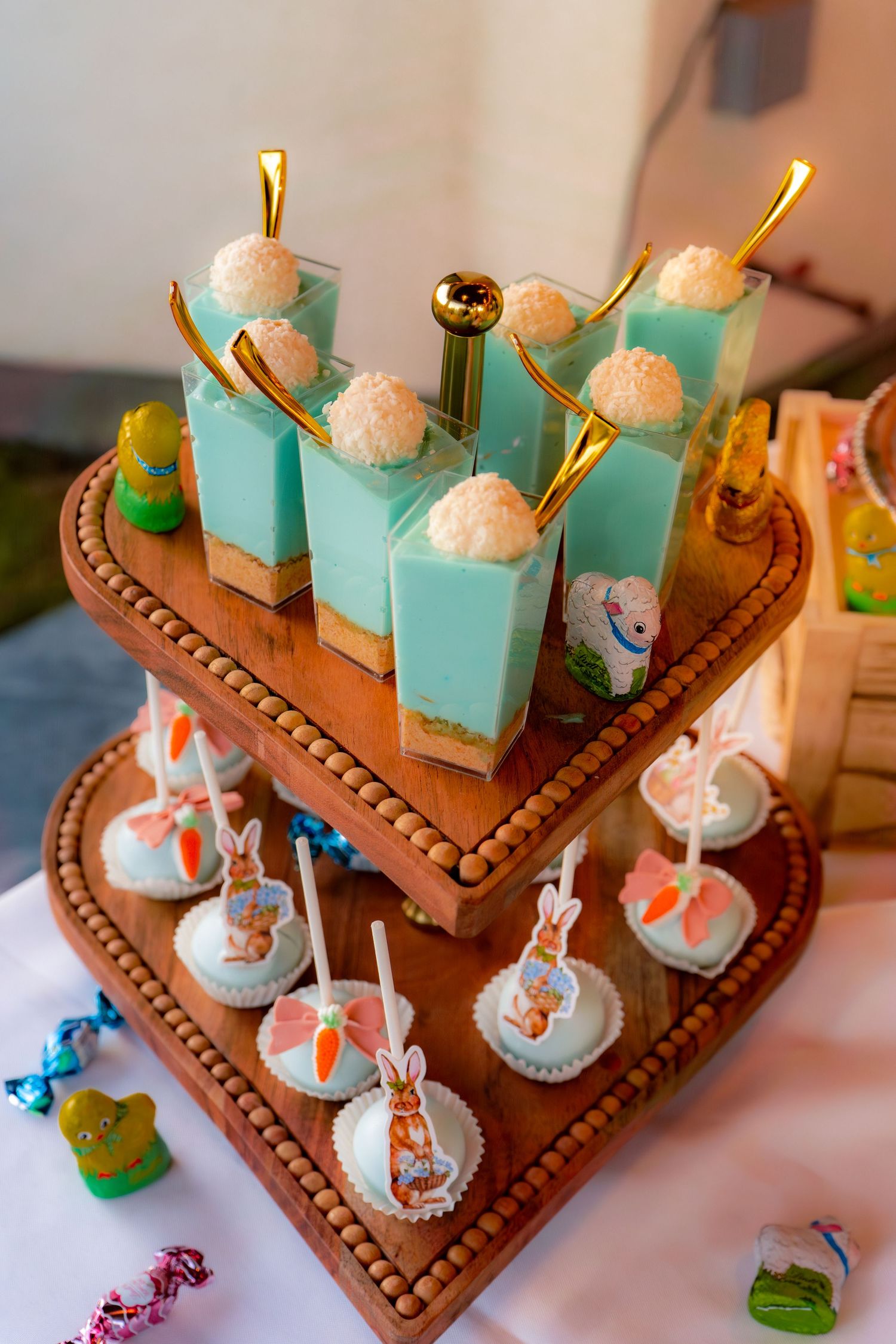 Tiered wooden heart-shaped stand with blue layered dessert cups and Peter Rabbit themed cake pops.