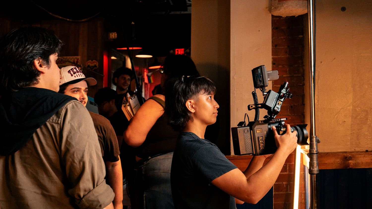 A camera operator films a scene while crew members observe in a dimly lit venue.