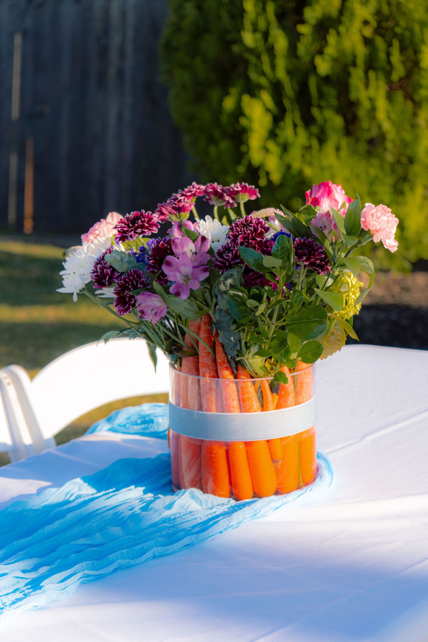 Creative baby shower centerpiece with carrots wrapped around a vase holding colorful mixed flowers.