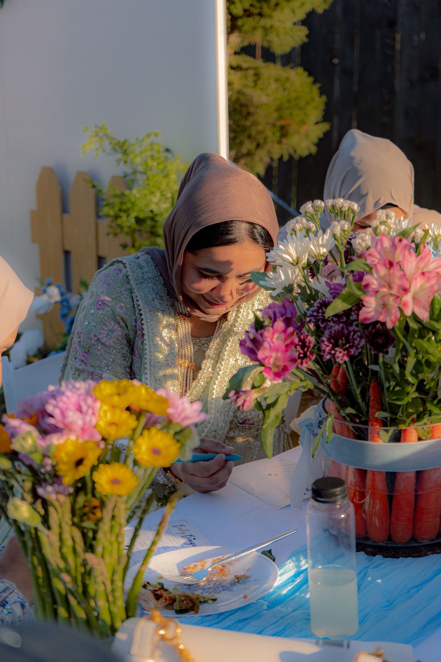Smiling woman in hijab enjoying a baby shower surrounded by colorful floral arrangements.