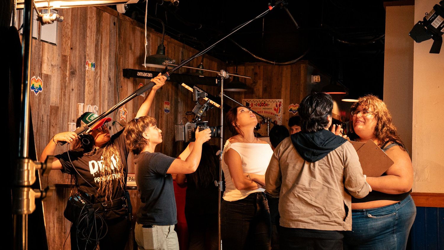 A film crew adjusts boom microphone and camera equipment on a rustic wooden set.