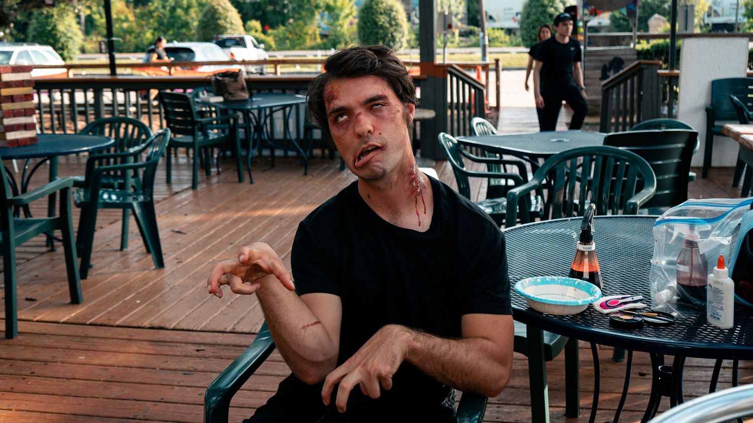Young man in black shirt sitting at an outdoor patio table gesturing during conversation.