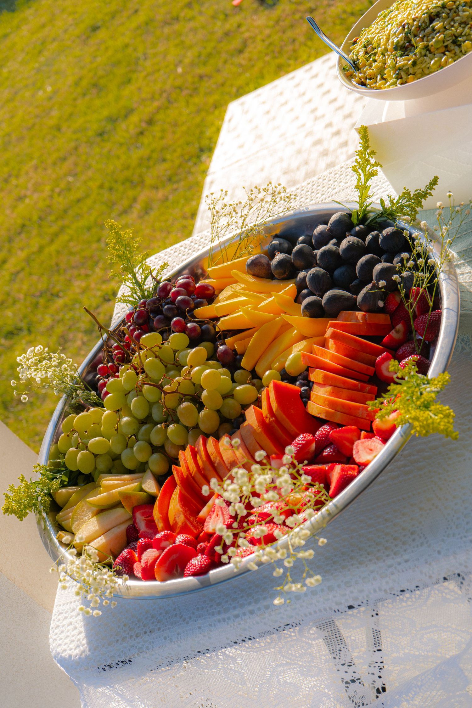 Colorful fruit platter with grapes, blueberries, strawberries, cantaloupe, and raspberries arranged in an oval silver tray.