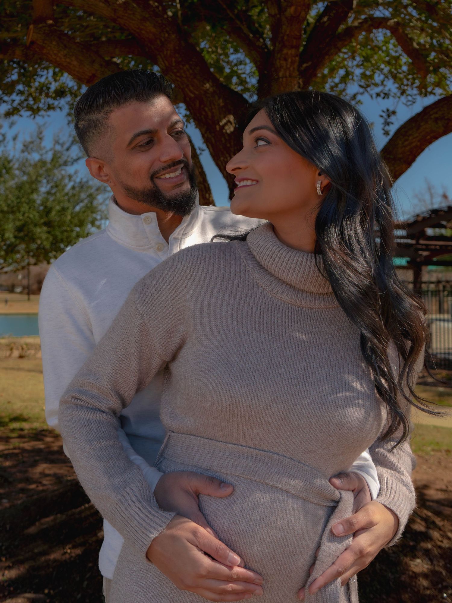 Loving couple posing for maternity photo outdoors both holding pregnant belly.