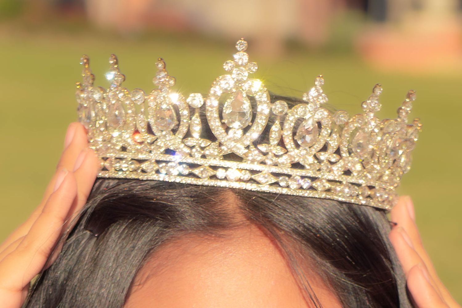 Close-up of a sparkling crystal tiara being placed on dark hair for a formal celebration or quinceañera.