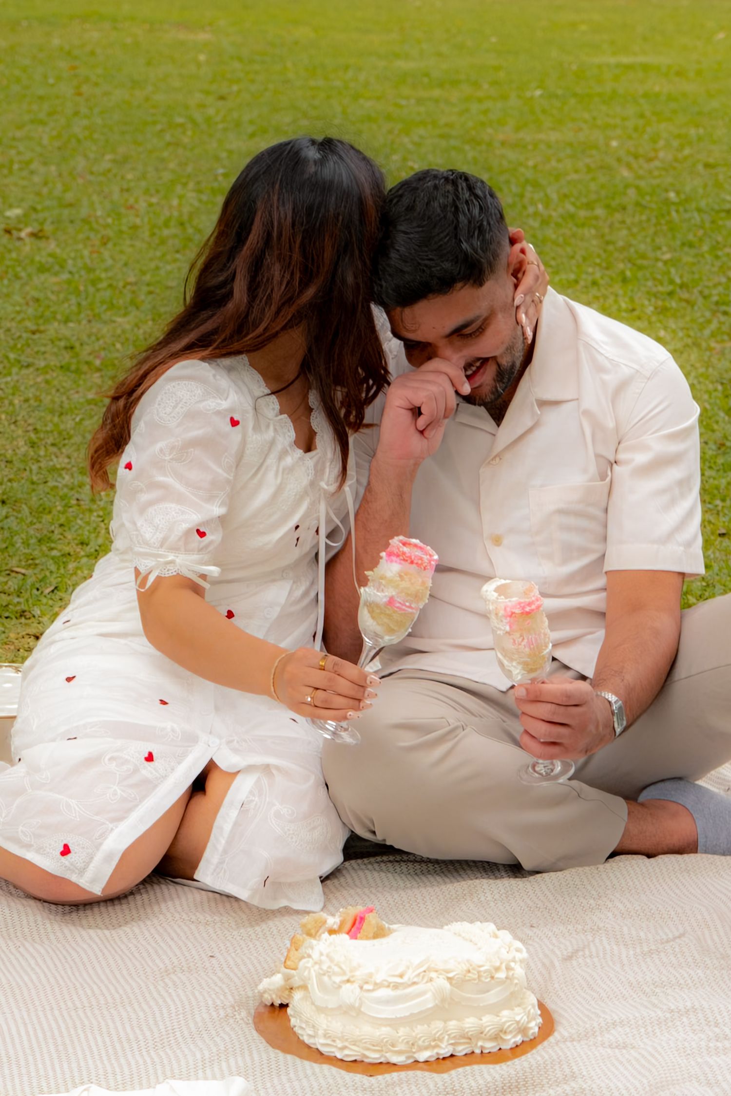 Couple sitting on blanket in park sharing cake and ice cream pops during maternity celebration.