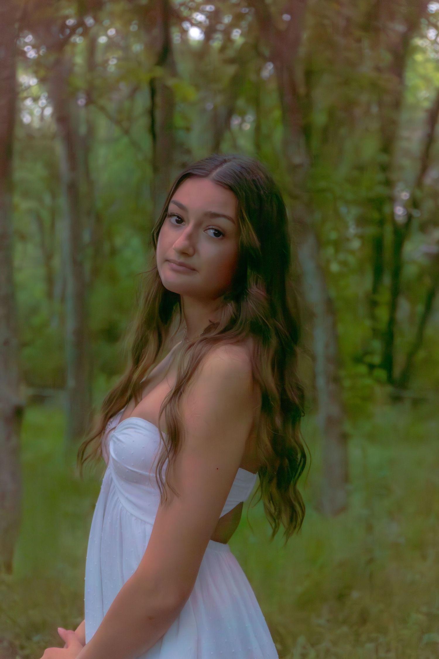 Young woman in white strapless dress posing gracefully among trees in a softly lit forest.